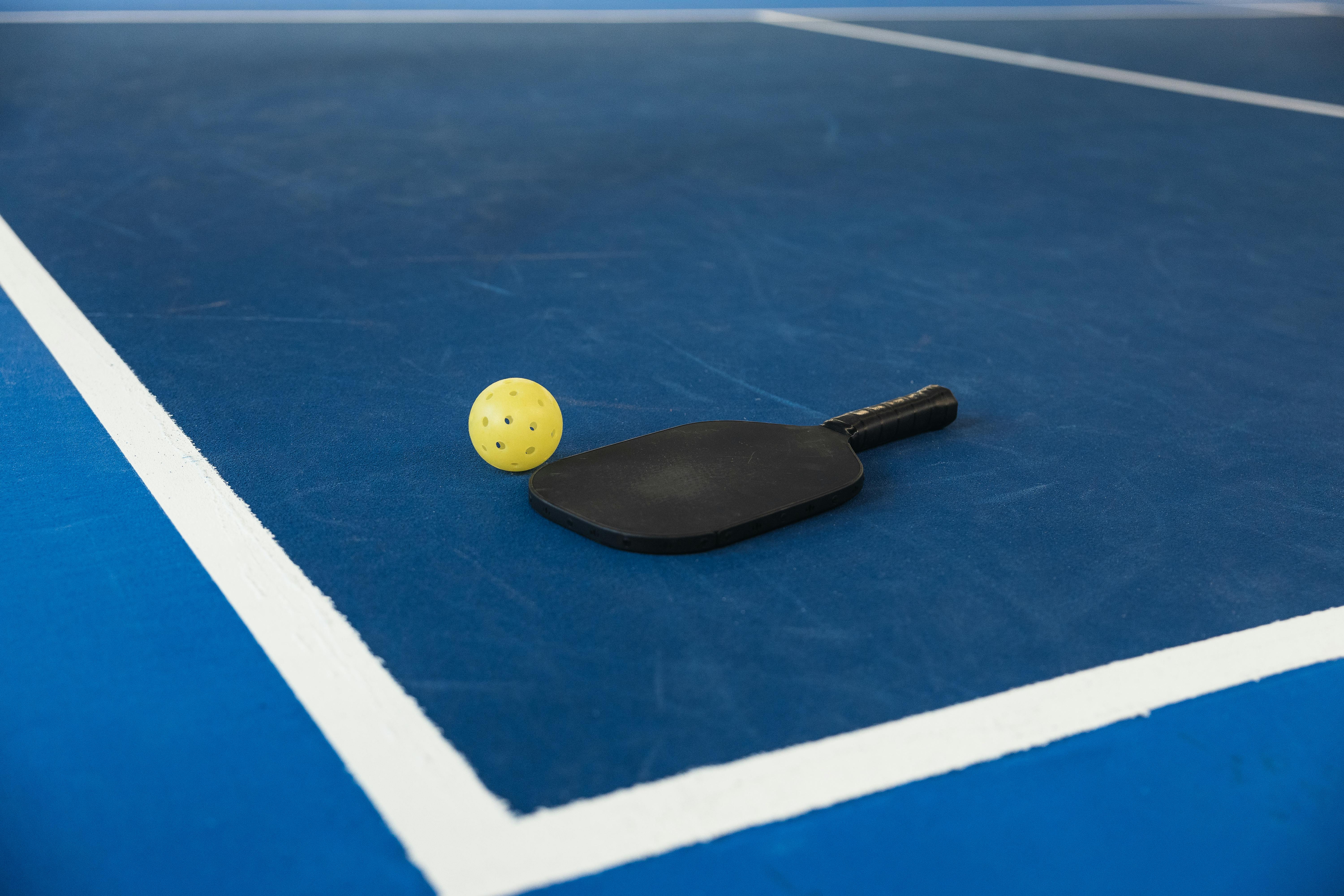 A pickleball paddle and ball on a pickleball court